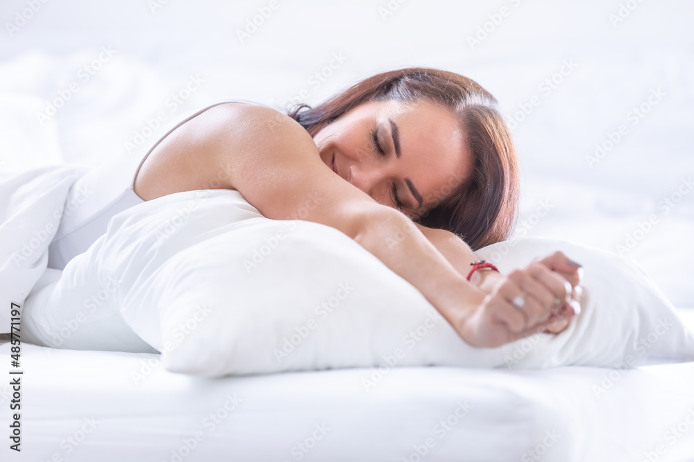 Woman lying on a large white pillow stretches as she wakes up smiling in the morning Woman lying on a large white pillow stretches as she wakes up smiling in the morning