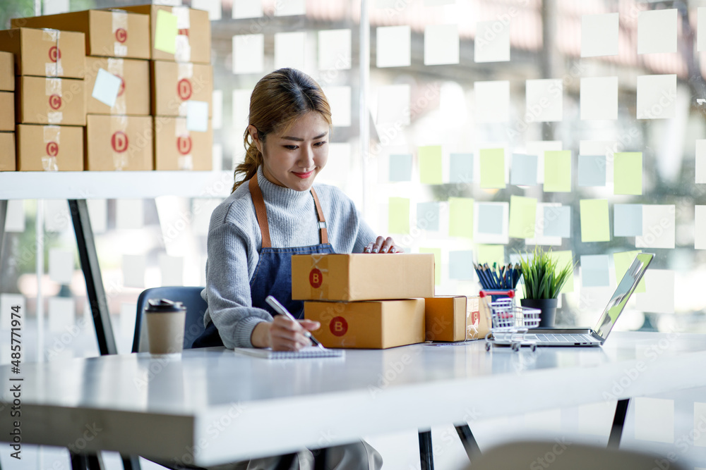 Startup SME small business entrepreneur SME or freelance Asian woman using a laptop with box, Young success Asian woman with her hand lift up, online marketing packaging box and delivery, SME concept. Startup SME small business entrepreneur SME or freelance Asian woman using a laptop with box, Young success Asian woman with her hand lift up, online marketing packaging box and delivery, SME concept.