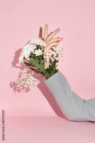 Fototapeta Naklejka Na Ścianę i Meble -  Spring creative layout with flowers and hand in jacket sleeve against pastel pink background. Romantic fashion aesthetic concept. Minimal bloom idea.