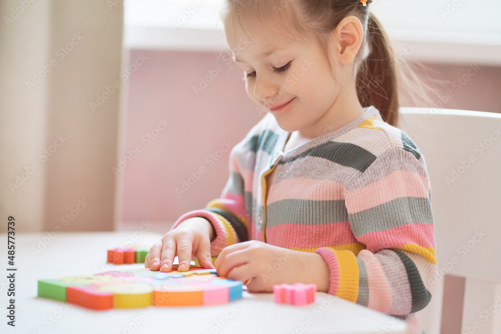 Little girl in colorful sweater plays with wooden puzzle at home. Little girl in colorful sweater plays with wooden puzzle at home.