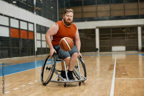 Male athlete in wheelchair plays basketball in sports hall.