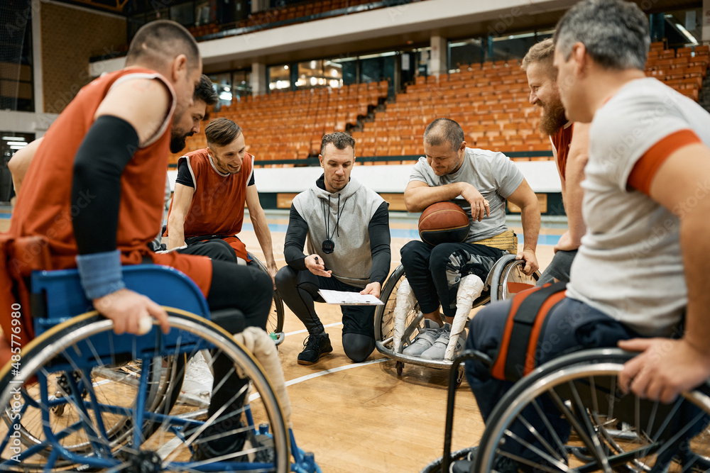 Obraz premium Coach of wheelchair basketball and his players with disabilities going through game strategy on the court.