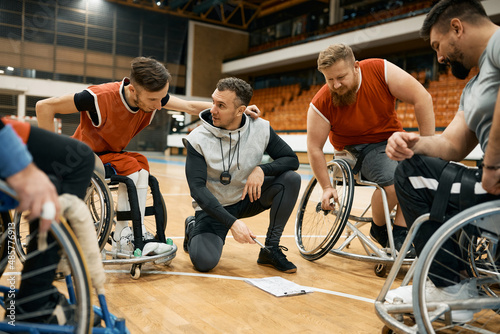 Basketball players in wheelchairs and their coach planning strategy before the match on sport court. photo