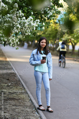 A young girl walks in the city park in the spring. Alley of blooming apple tree.  © Viktoriya