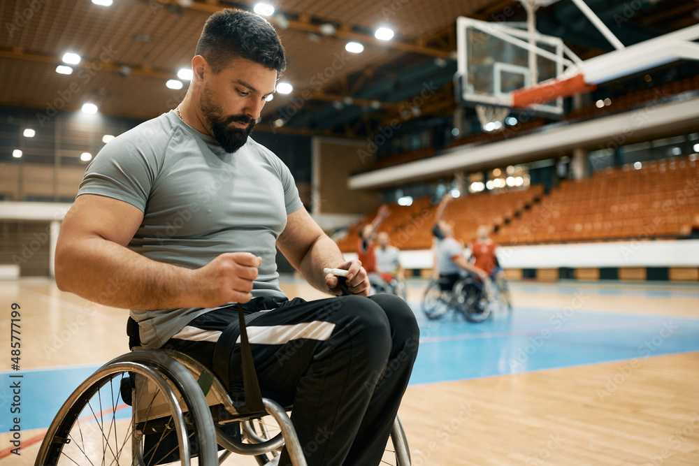 Obraz premium Basketball player with disability strapping his legs on wheelchair before sports training.