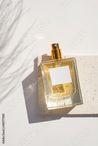 Transparent bottle of perfume with white label on stone plate on a white background. Fragrance presentation with daylight. Trending concept in natural materials with plant shadows. Women's and men's photo