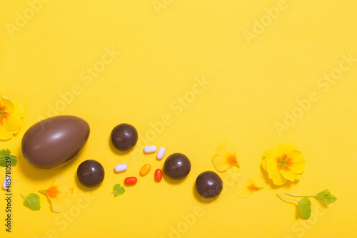 Easter yellow background with chocolatte eggs, candy and spring flowers