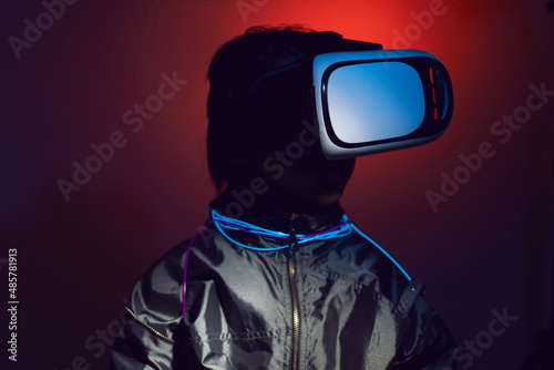 boy child in a silver jacket and glasses virtual reality playing a game. color of cyberpunk