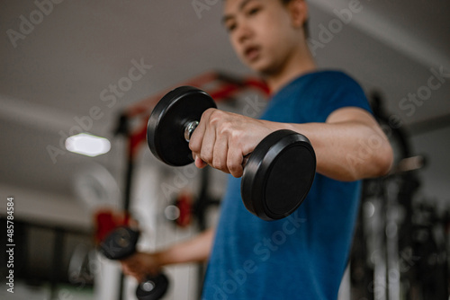 Training gym concept a young adult using his muscular strong arm lifting a dumbbell upward and downward in the gym