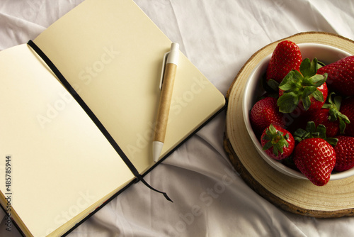 Blank notebook, pen and strawberries on white sheet. Flat lay, top view