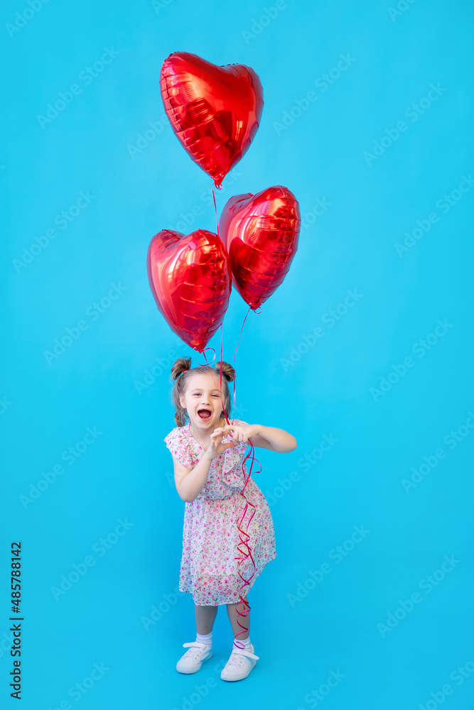 a little child girl on a blue isolated studio background with red balloons in the shape of a heart is having fun and fooling around. Space for copying text. Valentine's Day concept a little child girl on a blue isolated studio background with red balloons in the shape of a heart is having fun and fooling around. Space for copying text. Valentine's Day concept