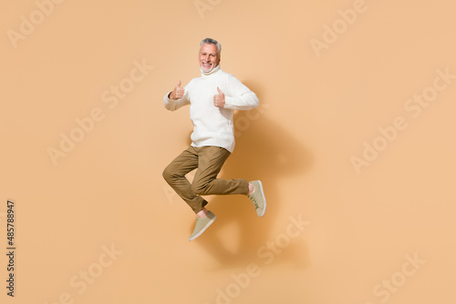 Full length body size view of attractive cheerful lucky man jumping showing thumbup isolated on beige pastel color background © deagreez