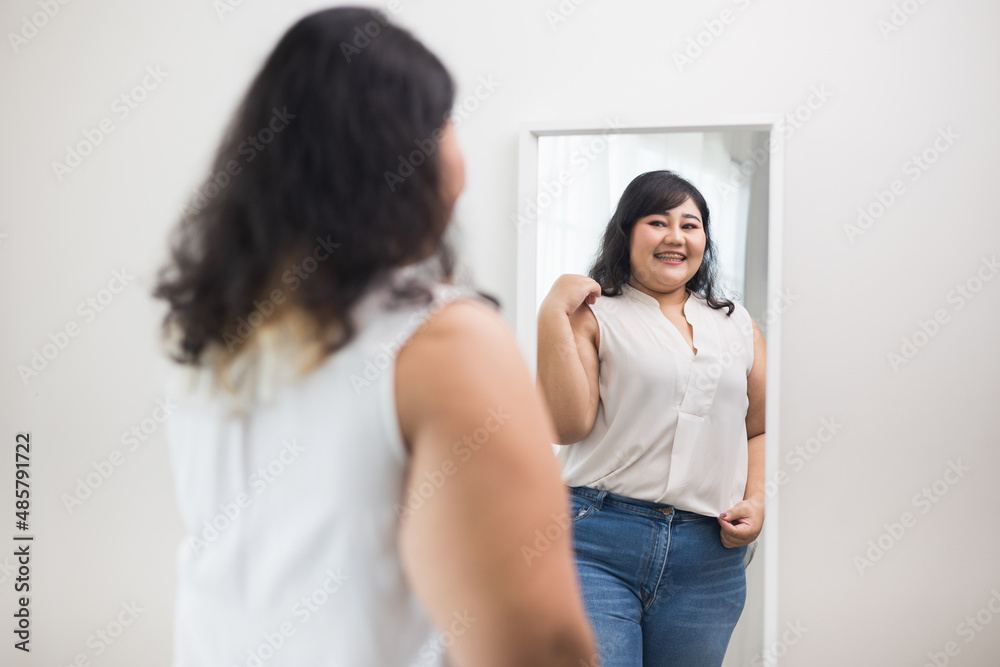 Body positive plus size female clothing. Body positive plus size woman happily and is proud of herself looking at mirror at home. Try wearing clothes that measure the size. Body positive plus size female clothing. Body positive plus size woman happily and is proud of herself looking at mirror at home. Try wearing clothes that measure the size.