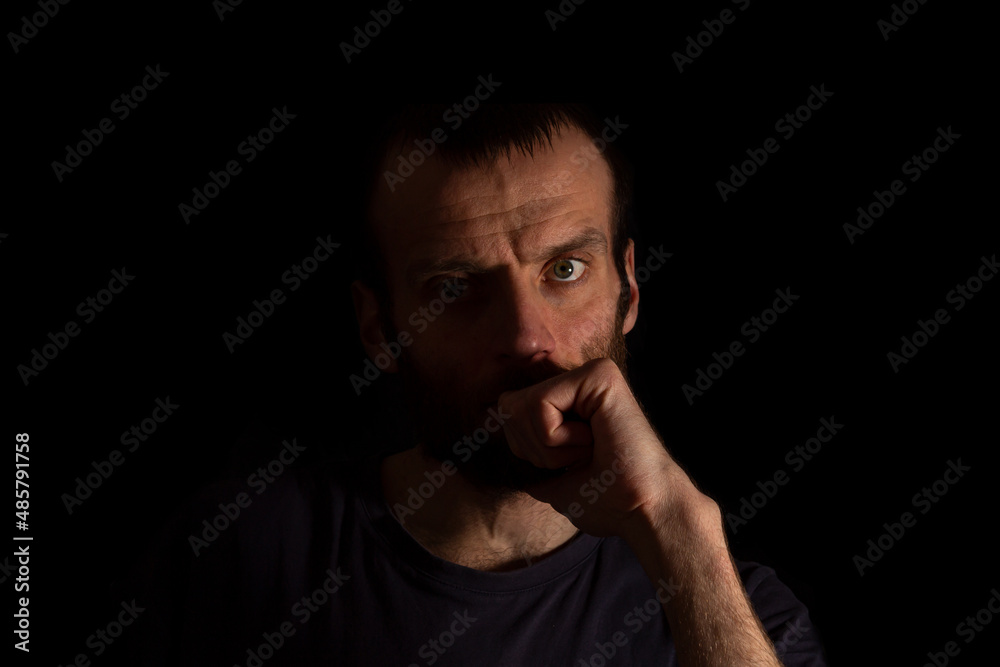 A concentrated man on a dark background in dark clothes holds his hand in front of him. Isolated from the background