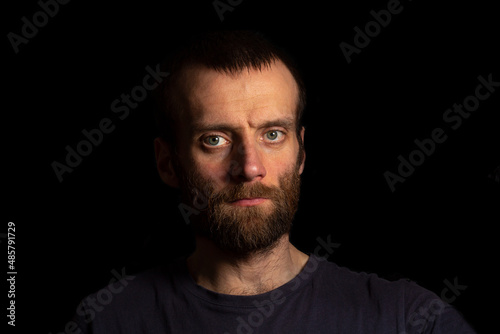 a man on a dark background in a dark T-shirt looks straight ahead. Isolated on a dark background.