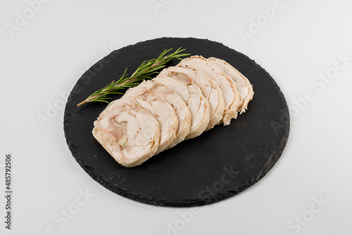 Pieces of pork roll with rosemary sprig on a black plate with a white background.