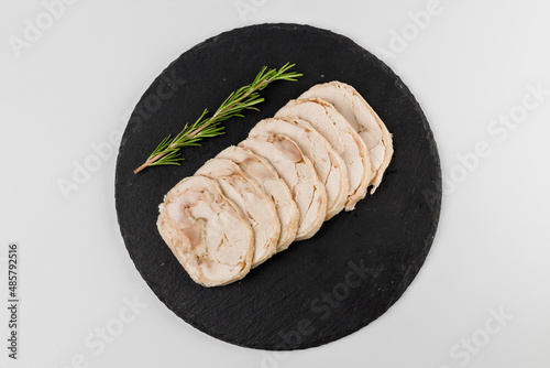 Pieces of pork roll with rosemary sprig on a black plate with a white background.