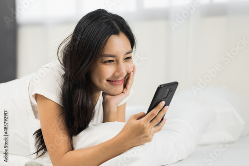 Pretty asian woman using smart phone on bed to social media at home in the morning. Lifestyle of young beautiful female using mobile phone to network internet online on the bed