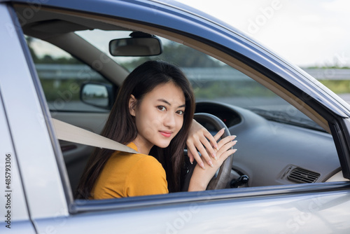 Young beautiful asian women getting new car. she very happy and excited. she sit and touching every detail of car. Smiling female driving vehicle on the road © Chanakon