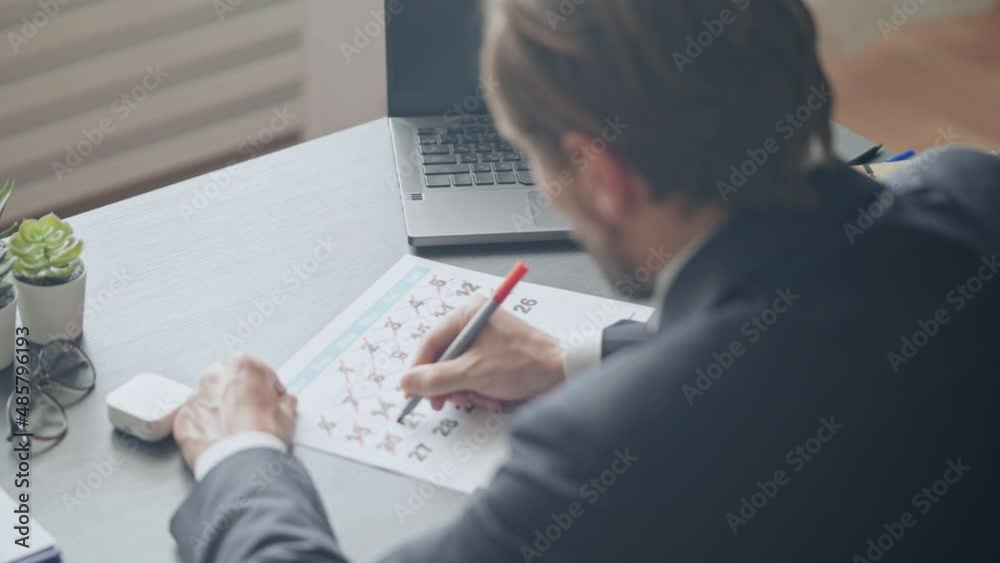 Businessman crossing and circling days in calendar, planning important meeting Businessman crossing and circling days in calendar, planning important meeting