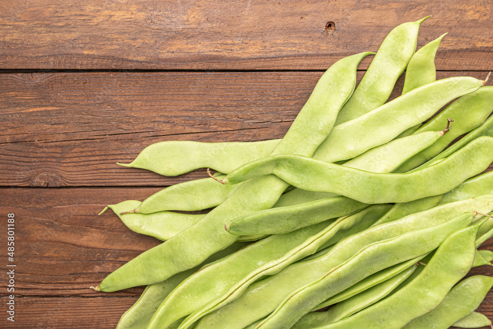 Raw green beans closeup. Fresh green bean also known as french beans, string beans, snap bean, snaps and haricots vert on wooden Raw green beans closeup. Fresh green bean also known as french beans, string beans, snap bean, snaps and haricots vert on wooden