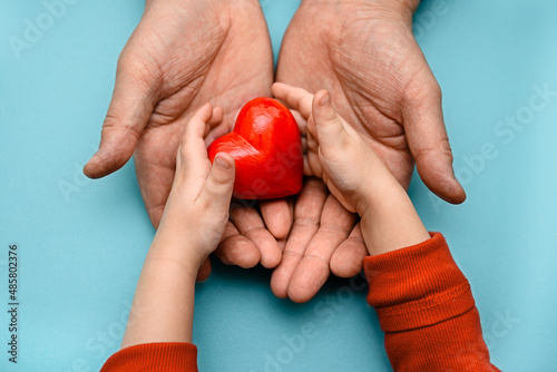 Fototapeta Naklejka Na Ścianę i Meble -  Adult and children's hands holding a red heart - the concept of health, love and family. Mother's Day, health Day. Adoption and charity.
