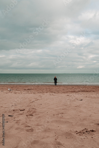 View out to sea from the beach in Swanage, England. A woman is standing at the edge of the sea in the distance. Turquoise teal sea and vibrant warm sand in foreground. Peaceful beach scene.