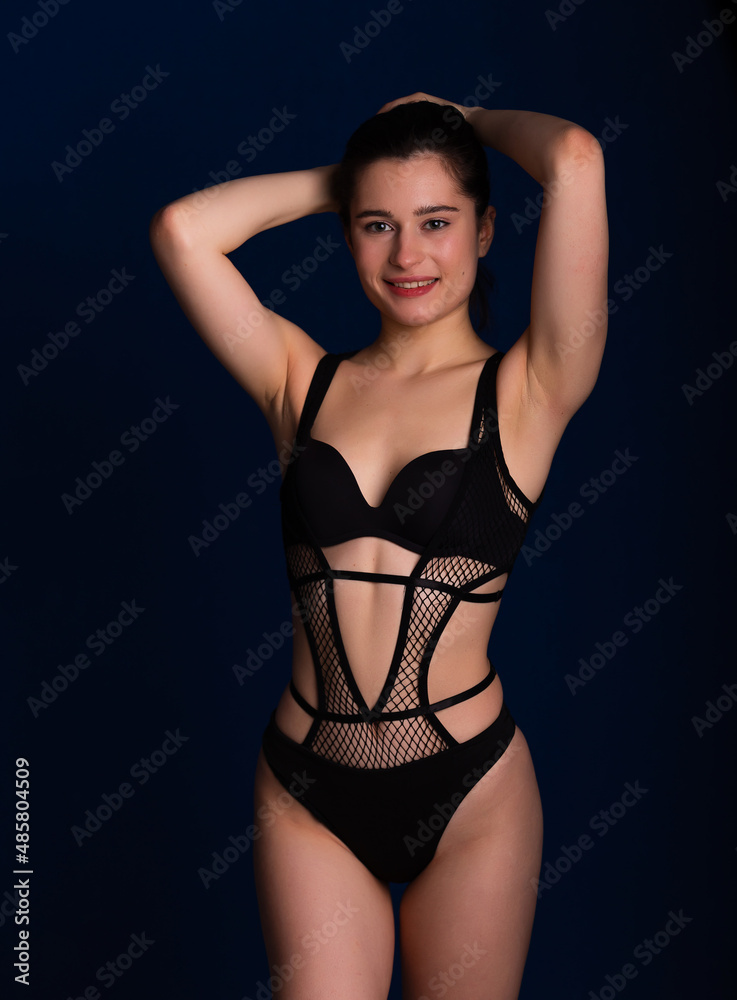 Fototapeta premium Woman posing in seductive black lingerie. Attractive beauty lady advertising underwear slim body on dark blue background free space for text