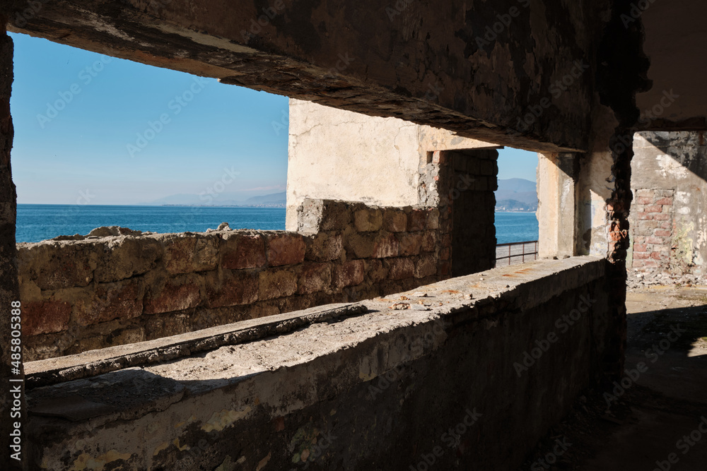 An abandoned concrete building on shores of beautiful blue sea awaiting demolition. Environmental impact. Coastal law. Financial crisis. Bankruptcy. Bankrupt construction company. Bright sun.