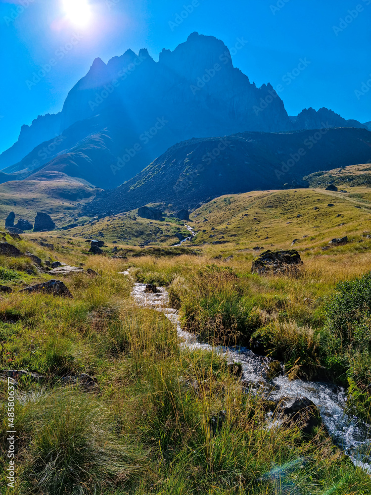 A panoramic view on a river flowing down a valley near the village in Roshka in the Greater Caucasus Mountain Range in Georgia, Kazbegi Region. Green alpine pasture. Wanderlust.