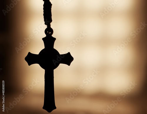 Close-up picture of a silhouette of a Rosary with a blurry background photo