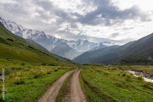 A hiking path leading to the Shkhara Glacier in the Greater Caucasus Mountain Range in Georgia, Svaneti Region, Ushguli. Snow-capped mountains in the back. Wanderlust. Wilderness. Overcast and clouds © Chris