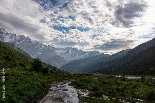 A hiking path leading to the Shkhara Glacier in the Greater Caucasus Mountain Range in Georgia  Svaneti Region  Ushguli. Snow-capped mountains in the back. Wanderlust. Ponds on the road from rain