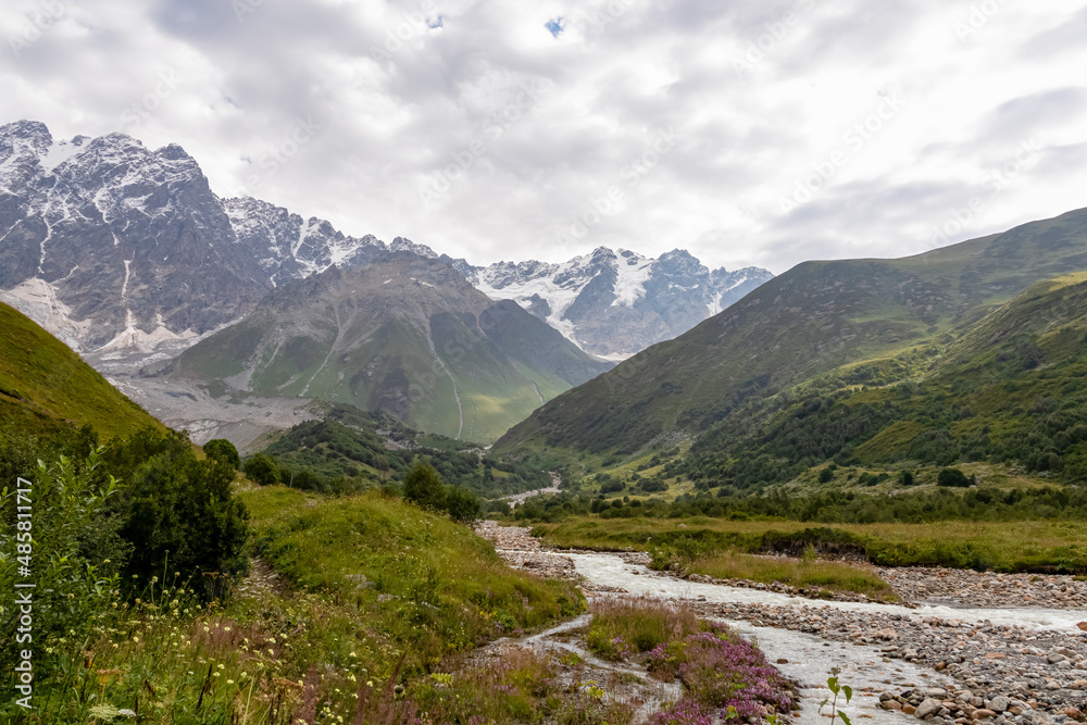 Patara Enguri River flowing down the a valley with view on the Shkhara Glacier in the Greater Caucasus Mountain Range in Georgia, Svaneti Region,Ushguli. Snow-capped mountains in the back. Wilderness.