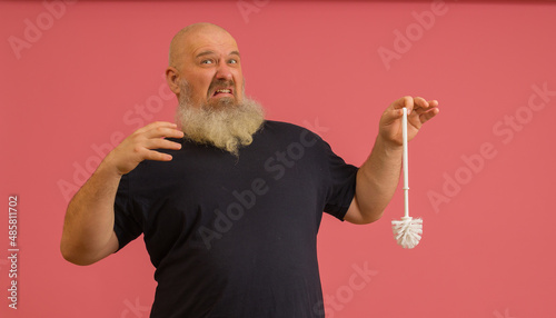 bearded man unpleasantly holding smelly toilet brush on pink background photo
