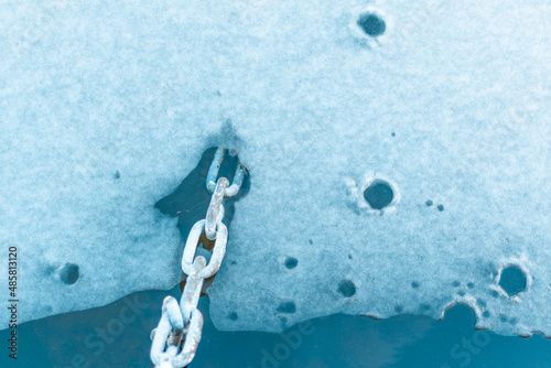 Metal chain on the melting ice shores of a frozen lake.Soft focus copy space.
