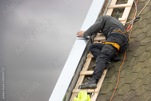 A man works on the roof repair, installs sheet metal on top of the gable wall