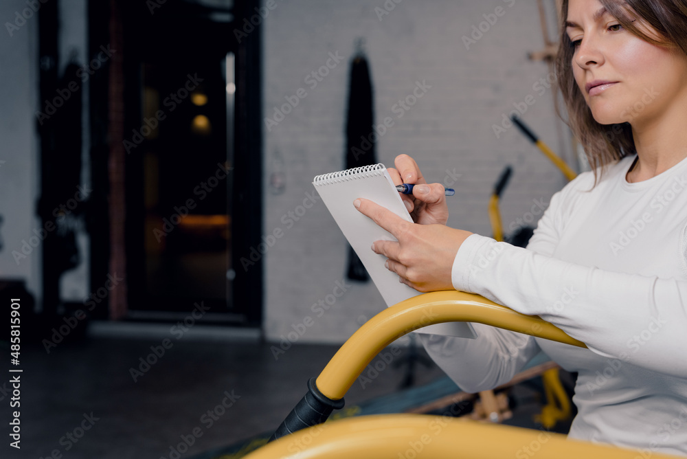 Adult fitness woman filling out workout planner in modern gym