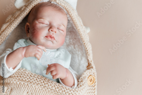 Reborn a boy doll sleeps in a knitted beige envelope. Copy space. photo