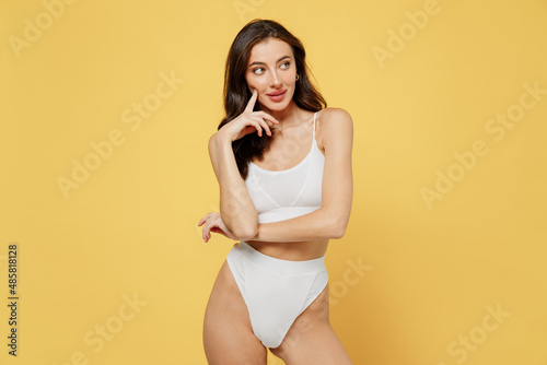 Minded gorgeous lovely attractive young brunette caucasian woman 20s wear white underwear with perfect fit body standing posing look aside isolated on plain yellow color background studio portrait © ViDi Studio