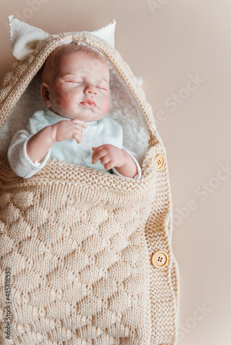 Bild auf Leinwand Reborn a boy doll sleeps in a knitted beige envelope