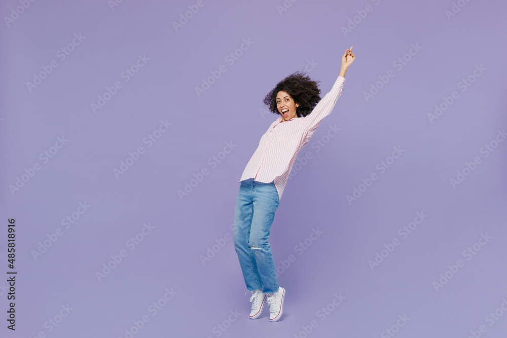 Full body side view young woman of African American ethnicity 20s in pink striped shirt lean back stand on toes dance fooling around isolated on plain pastel light purple background studio portrait