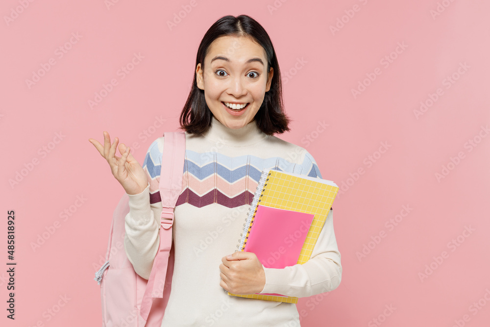 Surprised shocked fun teen student girl of Asian ethnicity wear sweater backpack hold books spread hands isolated on pastel plain light pink color background Education in university college concept. Surprised shocked fun teen student girl of Asian ethnicity wear sweater backpack hold books spread hands isolated on pastel plain light pink color background Education in university college concept.