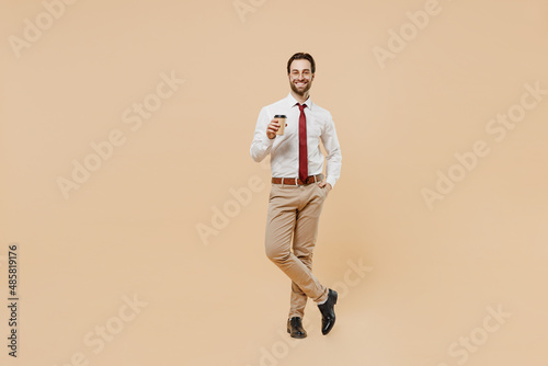 Full body young employee business man corporate lawyer 20s wear white shirt red tie glasses work in office hold takeaway delivery craft paper brown cup coffee to go isolated on plain beige background.