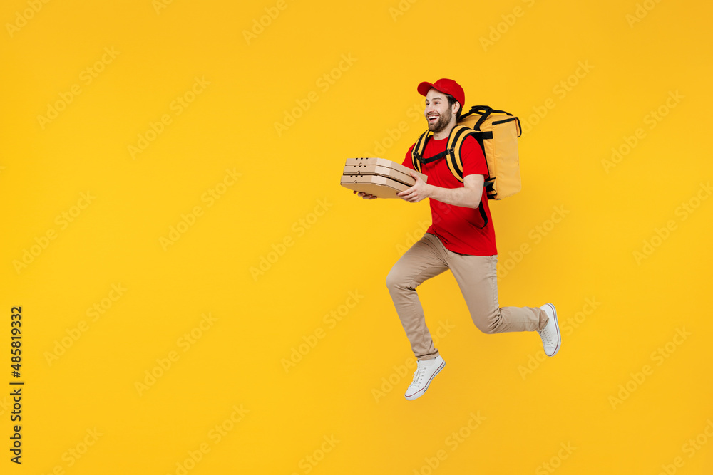 Side view full size delivery guy employee man in red cap T-shirt uniform work as dealer courier jump high hold cardboard box run fast jump thermal food bag backpack isolated on plain yellow background Side view full size delivery guy employee man in red cap T-shirt uniform work as dealer courier jump high hold cardboard box run fast jump thermal food bag backpack isolated on plain yellow background