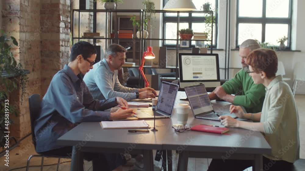 Businessmen and businesswomen using laptops, computer and taking notes while working at table in modern coworking space Businessmen and businesswomen using laptops, computer and taking notes while working at table in modern coworking space