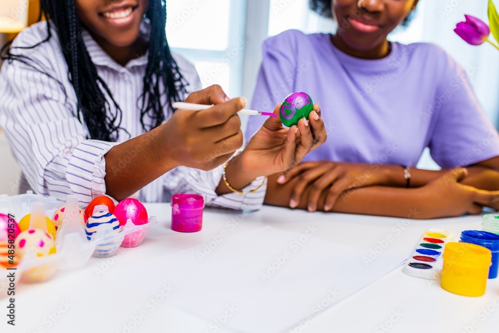multiracial two women painting eggs with cute pink rabbit costume ears in apartment multiracial two women painting eggs with cute pink rabbit costume ears in apartment