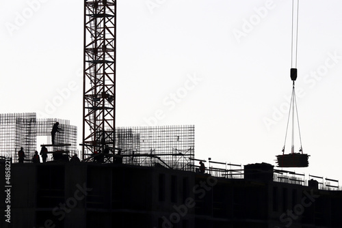 Silhouettes of workers and tower crane on construction site against the sky. Housing construction, builders working on scaffolding