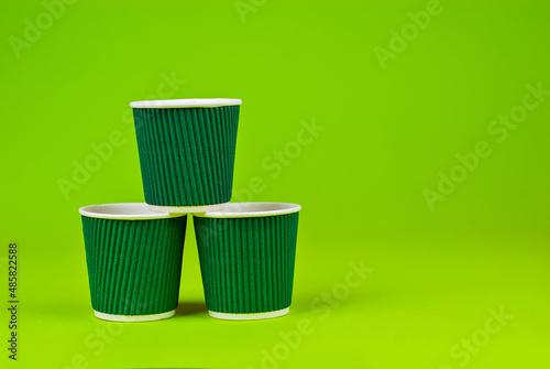 Disposable paper cups on a green background. Ecological coffee utensils. Copy space and free space for text near the glasses.