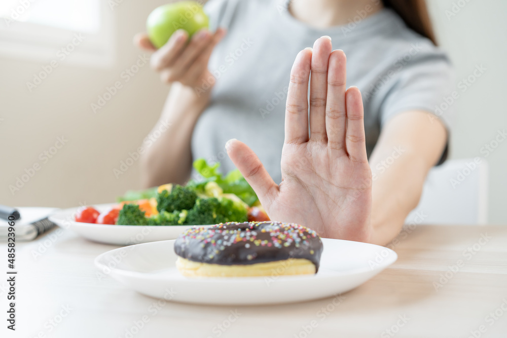 Diet, Dieting asian young woman or girl use hand push out, deny sweet donut and choose green salad vegetables, eat food for good healthy, health when hungry. Close up female weight loss person. Diet, Dieting asian young woman or girl use hand push out, deny sweet donut and choose green salad vegetables, eat food for good healthy, health when hungry. Close up female weight loss person.